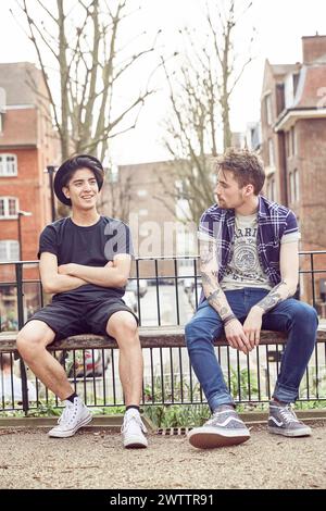 Two men sitting on a fence in an urban setting Stock Photo