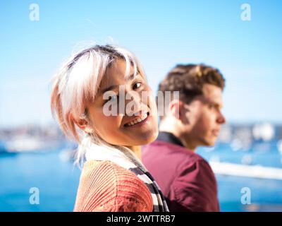Woman smiling with man in the background by the sea Stock Photo