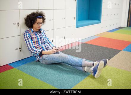 Man sitting on a colorful floor using a smartphone. Stock Photo