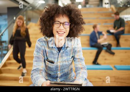 Smiling person with tablet sitting on stairs in a modern office Stock Photo