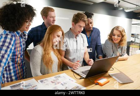 Team of six colleagues collaborating around a laptop Stock Photo
