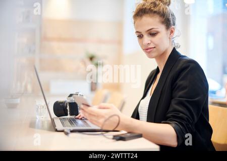 Woman using smartphone and laptop at a cafe Stock Photo