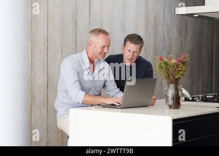 Two men working on a laptop in a modern kitchen Stock Photo