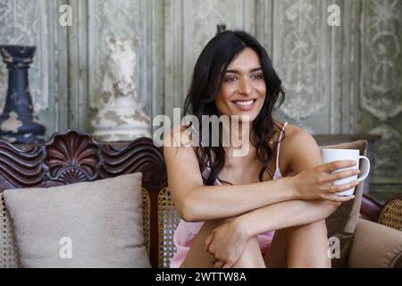 Woman smiling and holding a cup on a couch Stock Photo