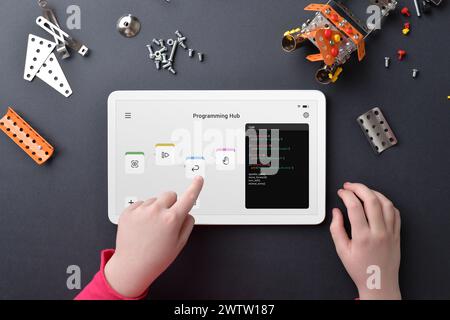 Child programing robot on tablet amidst small parts on work table. Illustrating education, programming skills, creativity, and hands-on learning Stock Photo