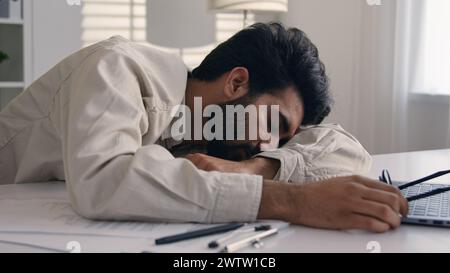 Lazy weary sleepy male manager tired exhausted Arabian Indian businessman employee working computer boring remote job man fall sleep on desktop Stock Photo