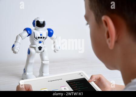Boy controls robot using tablet on desk. Illustrating education, technology, innovation, and interactive learning experiences in robotics and programm Stock Photo