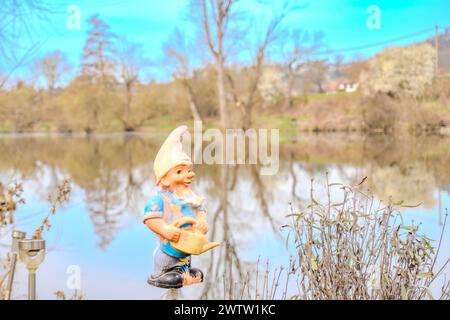 cute garden gnome, white beard, white cap and blue jacket stands in Early Spring Stock Photo