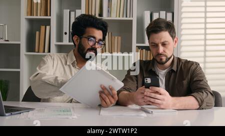 Two businessmen multiracial men co-workers in office Arabian Indian businessman show papers business project on laptop to colleague Caucasian man Stock Photo