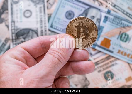 Trading with Bitcoin cryptocurrency, close up of male hand holding coin over US dollars, selective focus Stock Photo