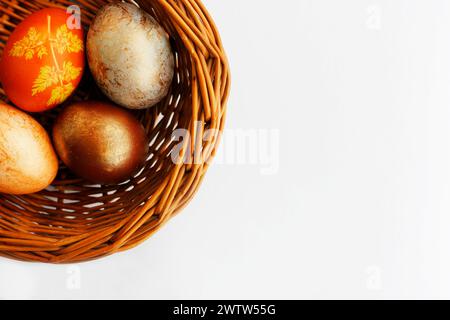 Four Easter eggs painted in different shades of brown color lying in a wicker basket on white background. Simple Easter flat lay in neutral colors wit Stock Photo