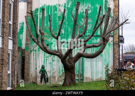 London, UK. 19th March, 2024. New artwork by world-renowned street artist Banksy which had appeared the previous day is pictured on the side of a residential building behind a tree located in the garden of a social housing block in Finsbury Park. The artwork, claimed by the street artist, takes the form of green paint sprayed onto a wall behind a pollarded cherry tree so as to appear like foliage when viewed from the front, together with a stencil of a woman holding a pressure washer. The shade of green paint used appears to match that used by Islington Council for its social housing signs. Cr Stock Photo