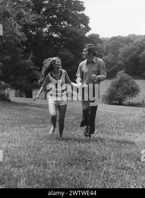 Young couple holding hands looking at each other happily while running through a field Stock Photo