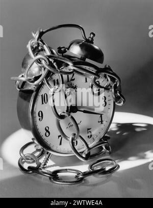 An image of an alarm clock with chains wrapped around it suggestive of time being stopped Stock Photo