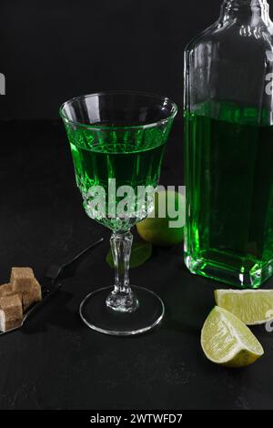 Absinthe, spoon, brown sugar and lime on black table. Alcoholic drink Stock Photo