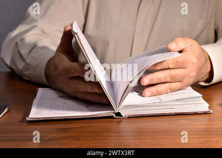A man sitting at a table flips through the pages of a notebook and reads the information. Stock Photo
