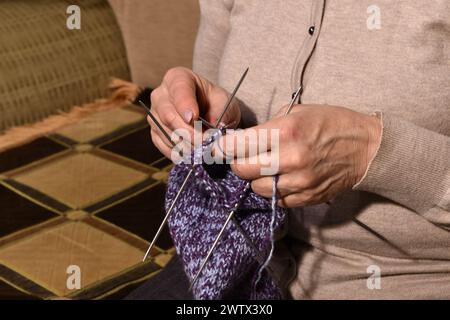 Close-up shot of the hands of an elderly woman. She is holding knitting needles and a woolen sock. Stock Photo