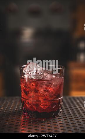 Close-up of a red cocktail with ice in a stylish glass, set on a dimly lit bar Stock Photo
