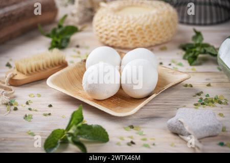 White bath bombs displayed elegantly on a bamboo plate, decorated with fresh mint leaves on a wooden background Stock Photo