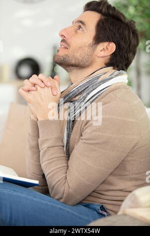 faithful middle aged man praying while sitting on sofa Stock Photo