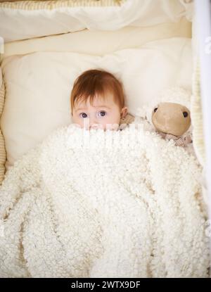 Baby, bed and blanket with sheep in home, above and healthy with growth, development and playing in morning. Infant, child and newborn with lamb doll Stock Photo
