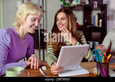 Two engaged female entrepreneurs - young women focused on a digital tablet in a modern home office setting - teamwork and productivity - planning and Stock Photo