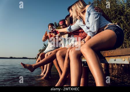 Group of friends sitting on the edge of a pier having fun and enjoying a summer day at the lake. Stock Photo