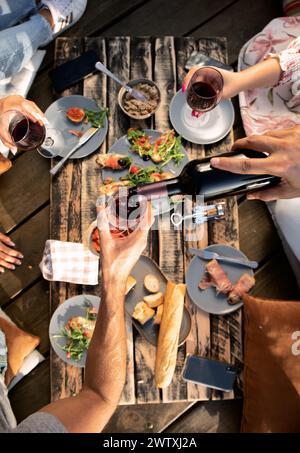 Close up of hand poring red wine in glass over food at picnic. Stock Photo