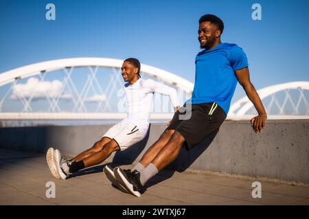 Two friends are exercising in the city. They are doing reverse push-ups. Stock Photo