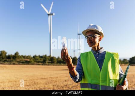 Electrical engineer holding energy saving light bulb on unfocused background of windmill. Stock Photo