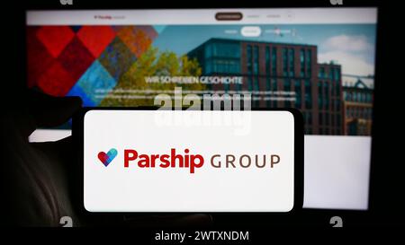 Person holding cellphone with logo of German online dating company ParshipMeet Holding GmbH in front of business webpage. Focus on phone display. Stock Photo