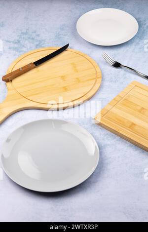 empty plates and serving and cutting boards on a light blue background, fork and knives nearby Stock Photo