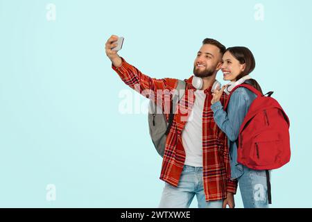 Cheerful college couple with smartphone snapping selfies against blue backdrop Stock Photo