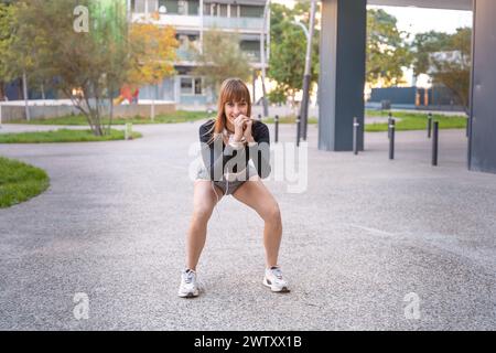 Active and fit female athlete doing squat exercise outdoors. Stock Photo