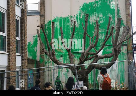 The Banksy artwork which has been defaced with white paint after it appeared over the weekend on the side of a residential building on Hornsey Road in Finsbury Park, London. Bright green paint has been sprayed on the building, in front of a cut-back tree, creating the impression of being its foliage. A stencil of a person holding a pressure hose has been sketched onto the building as well. The vivid paint colour matches that used by Islington Council for street signs in the area. Picture date: Wednesday March 20, 2024. Stock Photo