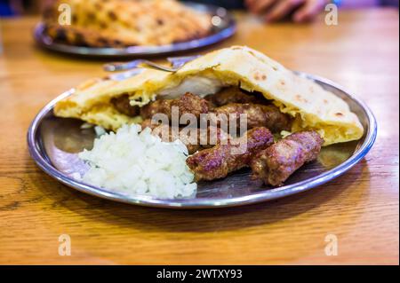 Traditional bosnian barbecue dish cevapi served with somun and chopped onions. Famous balkan BBQ dish served on an inox plate in Bascarsija, Sarajevo, Stock Photo