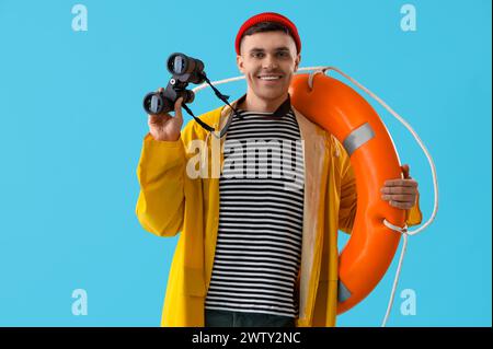 Young sailor with ring buoy and binoculars on blue background Stock Photo