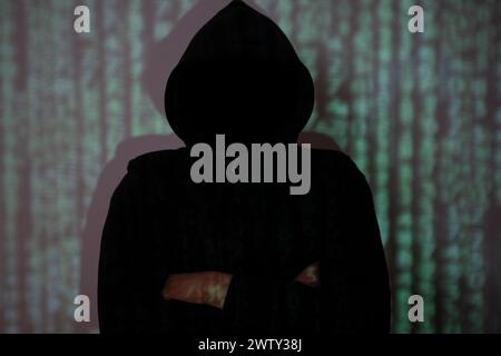 The hacker stood in the shadows with his arms crossed. Stock Photo