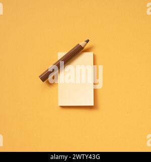 Blank memo notepad and brown pencil on orange desk background. top view, copy space Stock Photo