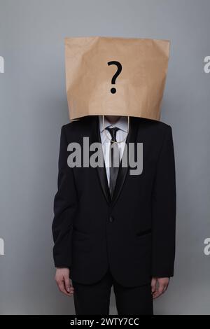 Person anonymous hiding his head behind paper bag with question mark against gray studio wall background Stock Photo