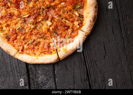 Italian pizza with several types of meat on a black wooden background, top view, copy space. Stock Photo