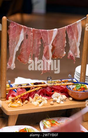 Original exquisite serving of meat snacks, jamon, ham, salami, assorted cheeses, olives, sauce. Antipasti on the table in a restaurant, Italian Stock Photo