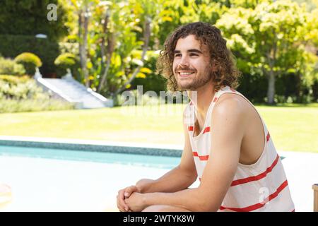 A young Caucasian man with curly brown hair smiles warmly, with copy space, at home outdoors Stock Photo