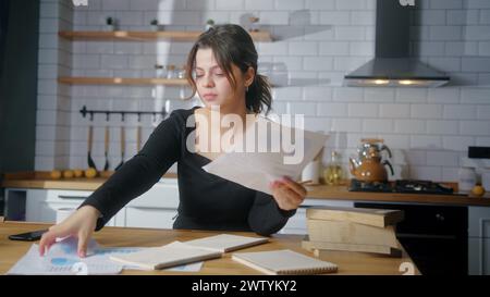 A college student sit in the kitchen studying, taking notes. Woman tired to study taking break. Study home concept Stock Photo