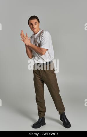 fashionable young male model in sophisticated pants looking at camera while on gray background Stock Photo