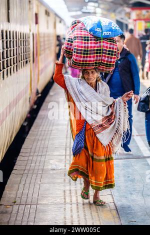An elderly Indian lady carrying goods on her head at a railway station Stock Photo