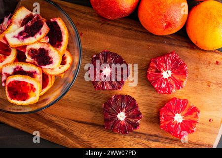 Peeled and Deseeded Blood Oranges on a Wooden Cutting Board: Peeled, halved, and whole raspberry oranges with peels on the side viewed from above Stock Photo