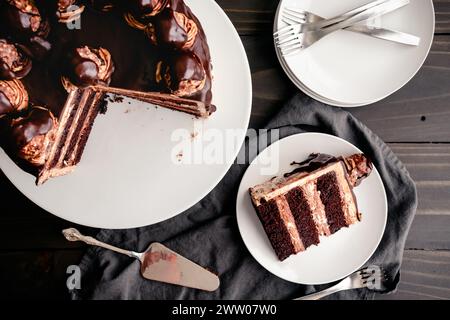 Sliced Hazelnut Chocolate Cake Topped with Ganache and Hazelnut Candies: Overhead view of a sliced chocolate layer cake on a table with plates Stock Photo