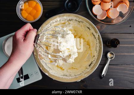 Hand Holding a Stand Mixer Whisk Attachment Covered in Buttercream: Woman's hand holding a wire whip covered in Swiss meringue buttercream frosting Stock Photo