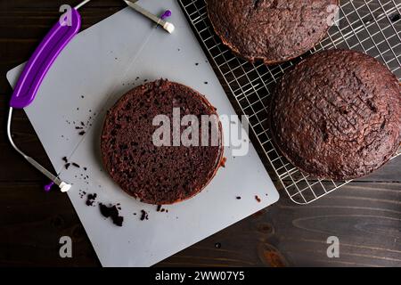 Leveling Round Chocolate Cakes to an Even Height: Round dark chocolate cakes being leveled with a wire cake leveler after cooling on a wire rack Stock Photo